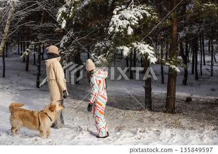 Two teenage girls playing with Golden Retriever under snowy pine tree in winter forest, joyful outdoor family moment with falling snow and nature Two teenage girls playing with Golden Retriever under snowy pine tree in winter forest, joyful outdoor family moment with falling snow and nature 135849597