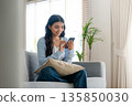 Smiling pretty young Asian woman sitting on cozy couch 135850030
