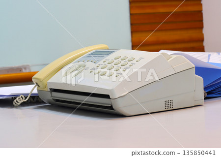 A fax machine on a desk with paper loaded, ready to send documents in an office setting 135850441