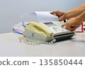 Man hands using a fax machine, putting paper in and sending fax in office 135850444