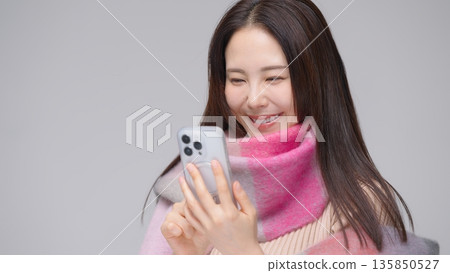 一位三十多歲的女子戴著圍巾，正在看她的智慧型手機。 135850527