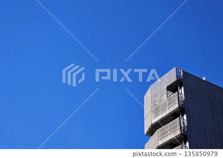 Minimal low angle view of the upper portion of a modern building against a clear blue sky. Minimal low angle view of the upper portion of a modern building against a clear blue sky. 135850979