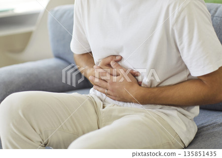 Sick man holding belly with hands, suffering from stomach pain, abdominal cramps Sick man holding belly with hands, suffering from stomach pain, abdominal cramps 135851435