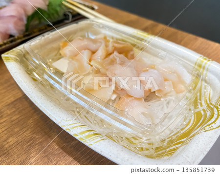 A plastic container filled with fresh clam sashimi. 135851739