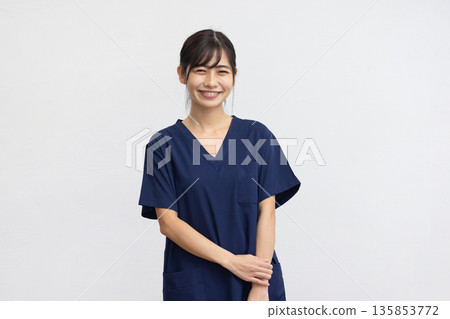 A young woman wearing a navy blue medical scrub and smiling in front of a white background A young woman wearing a navy blue medical scrub and smiling in front of a white background 135853772