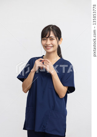 A young woman wearing a navy blue medical scrub and smiling in front of a white background A young woman wearing a navy blue medical scrub and smiling in front of a white background 135853778
