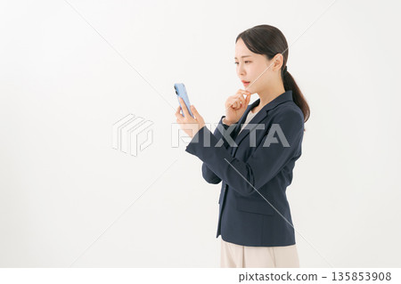 一位身穿西裝的女士看著她的智慧型手機，神情憂慮。 135853908