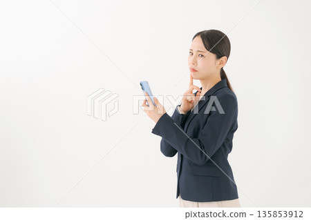 一位身穿西裝的女士看著她的智慧型手機，神情憂慮。 135853912