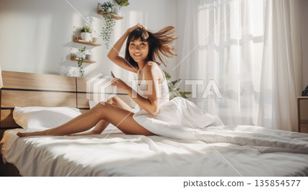 一位二十多歲、留著短髮的女子在晨光中伸展身體。她穿著白色睡衣，神清氣爽地醒來。 135854577