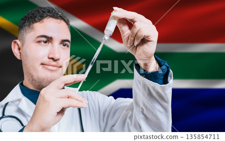 Doctor holding syringe on South Africa flag background. Medical professional holding syringe with South African flag in the background 135854711