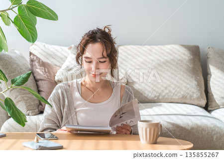 A stylish Asian woman sitting on the sofa in the living room and reading a magazine 135855267