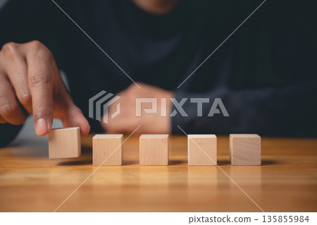 Hand placing wooden blocks in a row on a table.  Business strategy, planning, and growth concept. 135855984