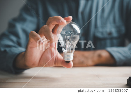 A hand holds a lightbulb over a wooden table, symbolizing new ideas and innovation. A hand holds a lightbulb over a wooden table, symbolizing new ideas and innovation. 135855997