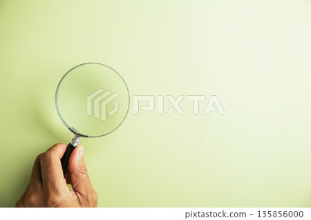 Hand holding a magnifying glass on a light green background. Perfect for search, investigation, or discovery concepts. 135856000