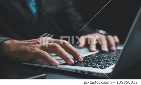 Close-up of hands typing on a laptop keyboard. The image focuses on the hands and the keyboard, with a blurry background. Close-up of hands typing on a laptop keyboard. The image focuses on the hands and the keyboard, with a blurry background. 135856012