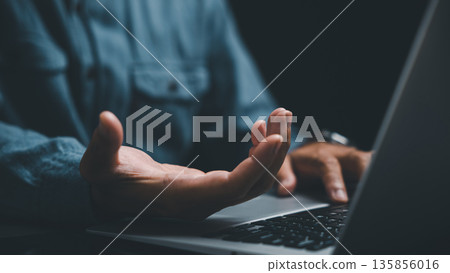 Close-up of hand on laptop keyboard, fingers typing, dark blue shirt in the background. 135856016