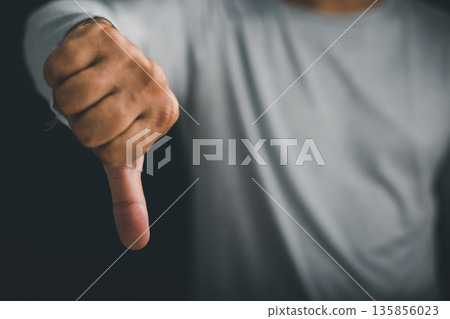 Closeup of a man hand pose with a thumbs down sign, a gesture showing dislike and a clear sign of disagreement or negative feedback on a dark and simple isolated background 135856023