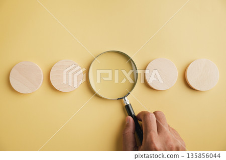 A magnifying glass on a yellow background with four round pieces of wood around it. 135856044