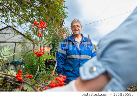 two farm workers talking. Senior man worker on organic farm. Portrait of male person in work uniform. Concept of manual labor and farming in rustic area. two farm workers talking. Senior man worker on organic farm. Portrait of male person in work uniform. Concept of manual labor and farming in rustic area. 135856593