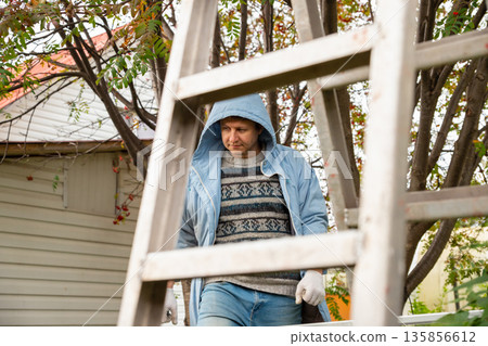 Organic farm worker and a metal stepladder. Hardworking labor, manual labor and farming. Maintenance and outdoor work. Organic farm worker and a metal stepladder. Hardworking labor, manual labor and farming. Maintenance and outdoor work. 135856612