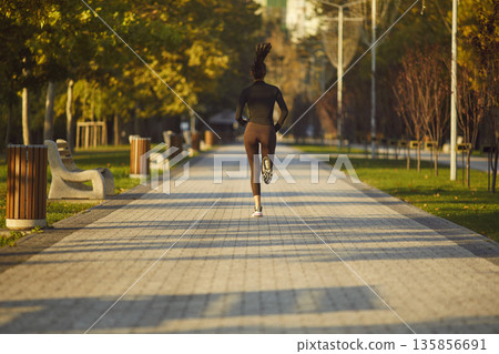 Young woman jogging in autumn park, active fitness training on sunny morning 135856691