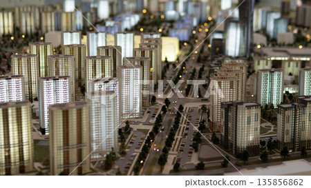 A detailed display shows a modern city layout with numerous buildings, streets, and green spaces. This real estate model highlights structures characteristic of the district. A detailed display shows a modern city layout with numerous buildings, streets, and green spaces. This real estate model highlights structures characteristic of the district. 135856862