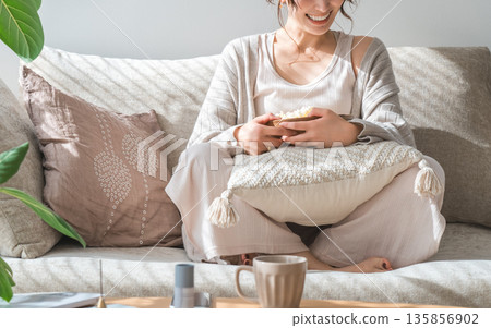 Smiling Asian woman sitting on the sofa in the living room and eating popcorn 135856902