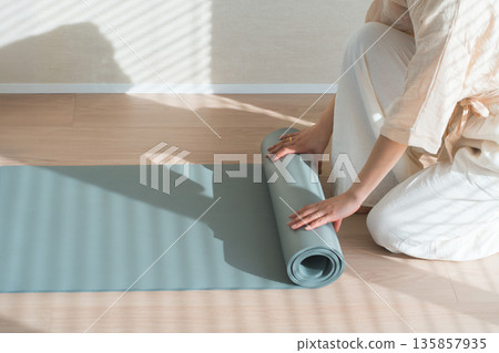 A woman's hands spreading and tidying up a yoga mat in the living room at home A woman's hands spreading and tidying up a yoga mat in the living room at home 135857935
