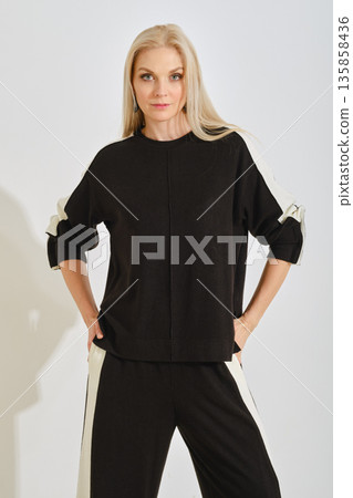 Woman in stylish black and white outfit poses confidently in a well-lit indoor space 135858436