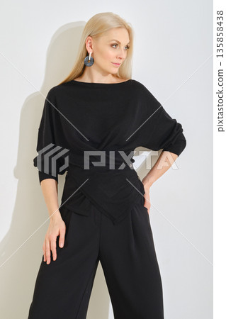 Chic black outfit featuring wrap top and wide-leg pants in stylish indoor setting 135858438