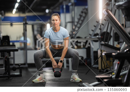 Woman exercising with kettlebell doing squats in gym Woman exercising with kettlebell doing squats in gym 135860093
