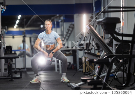 Woman training with kettlebell doing squats in gym Woman training with kettlebell doing squats in gym 135860094