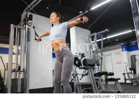 Woman exercising chest with cable crossover machine in gym 135860112