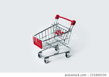 A miniature shopping cart rests on a clean white surface, side view A miniature shopping cart rests on a clean white surface, side view 135860330