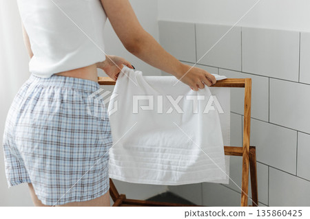 Woman put white towel on wooden hanger clothes rack in bathroom 135860425