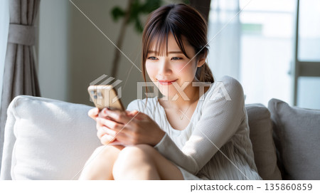 年輕女子在家中沙發上輕鬆地看著智慧型手機，展現了她輕鬆的日常生活。 135860859