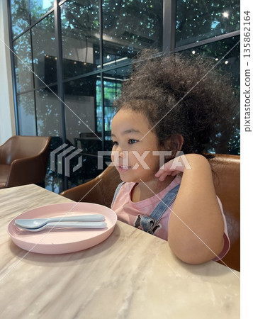 Cute Asian little girl sitting on a chair in a cafe. 135862164