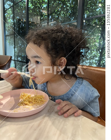 Cute little girl eating spaghetti with spoon in the kitchen in a restaurant. Healthy eating concept. 135862281