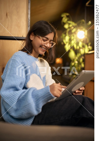 Smiling woman using tablet while working in cozy modern office lounge. Smiling woman using tablet while working in cozy modern office lounge. 135862477