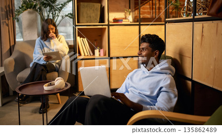 Young professionals working remotely in cozy modern office lounge. Young professionals working remotely in cozy modern office lounge. 135862489