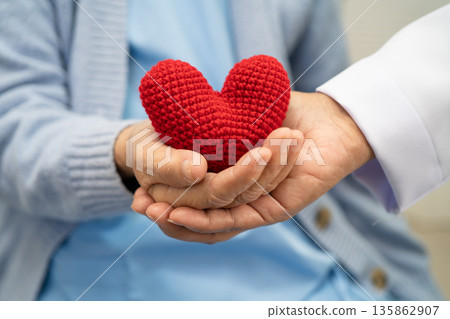 Doctor giving a red heart to senior patient in hospital. Doctor giving a red heart to senior patient in hospital. 135862907