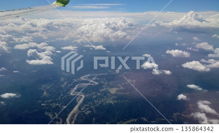 A sea of clouds and a great river flowing through the mountains seen from the airplane window 135864342