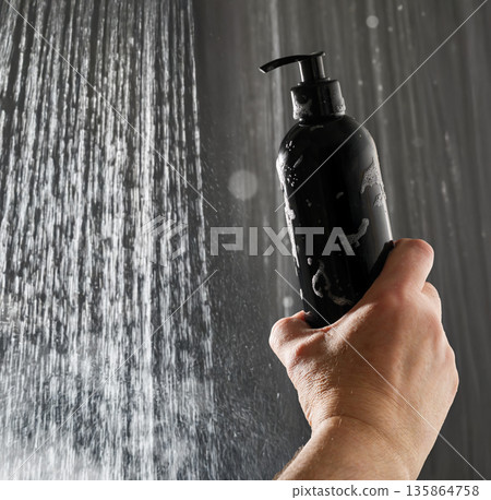 Hand holding black shampoo pump bottle in the shower 135864758