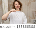 Woman holding a bamboo toothbrush with toothpaste, ready to begin her morning dental hygiene routine in the bathroom 135866388