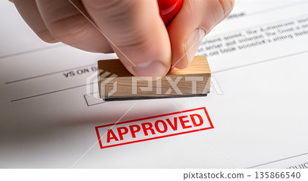 Hand holding wooden rubber stamp pressing approved word in red ink on paper document business contract agreement permission success finance deal Hand holding wooden rubber stamp pressing approved word in red ink on paper document business contract agreement permission success finance deal 135866540