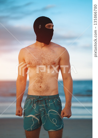 incognito white man in face mask with athletic muscular body standing at beach at sunny sunset, anonymous private attractive male athlete walking at sea or ocean shore incognito white man in face mask with athletic muscular body standing at beach at sunny sunset, anonymous private attractive male athlete walking at sea or ocean shore 135866780