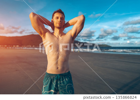 handsome white man with athletic muscular body standing at beach at sunny sunset, attractive male athlete walking at sea or ocean shore handsome white man with athletic muscular body standing at beach at sunny sunset, attractive male athlete walking at sea or ocean shore 135866824