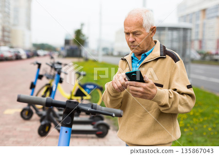 Grandfather wants to ride an electric scooter and pays rent with mobile phone Grandfather wants to ride an electric scooter and pays rent with mobile phone 135867043