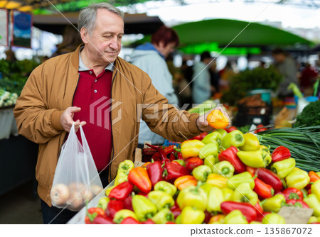 Casual senior male customer choosing organic vegetables while walking at local market 135867072