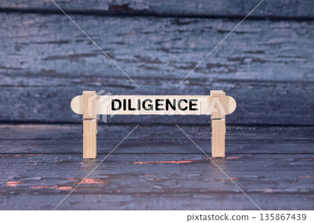 Diligence symbol. Wooden stick fastened by Clothespins, A lightly orange toned grunge wooden background. Business and Diligence concept with copy space 135867439